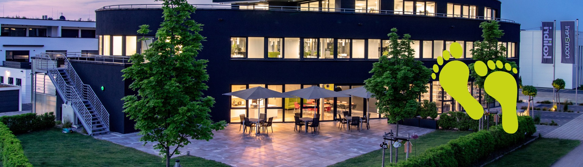 Dienstgebäude von der Firma Kolibri bei Sonnenuntergang mit einem abgebildeten grünen Fußabdruck der für Nachhaltigkeit steht